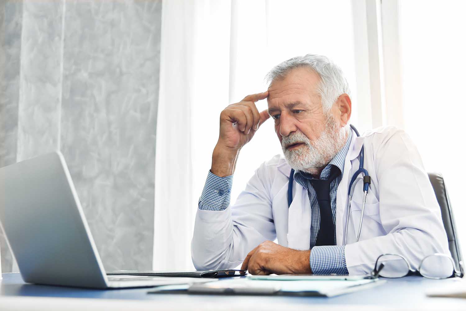 doctor looking at cancelled malpractice insurance policy on laptop