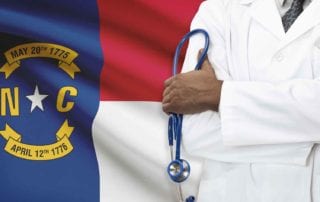 A Doctor With Liability Insurance Standing In Front Of A North Carolina Flag Holding A Stethoscope