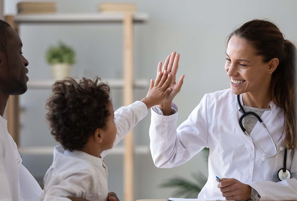 A Female Doctor Covered By A Malpractice Liability From MEDPLI Gives A High Five To A Small Child Held In His Caregiver's Lap
