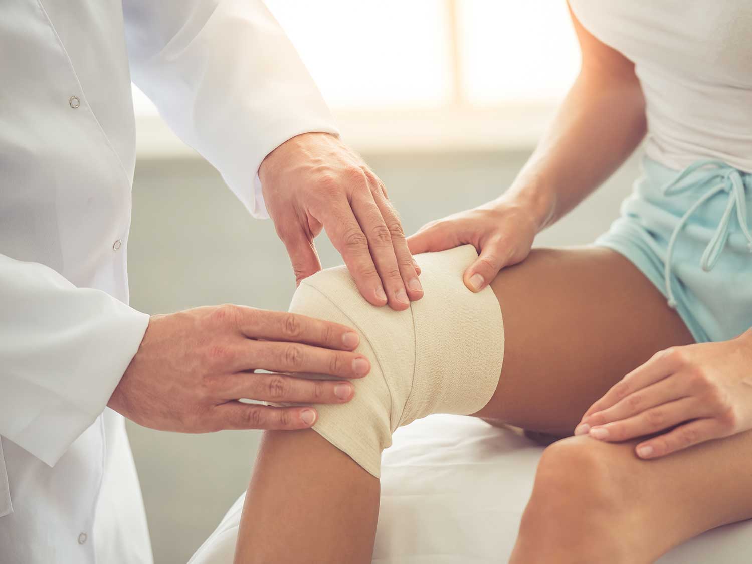 An Orthopedic Surgeon With Liability Coverage Examining The Bandaged Knee Of A Patient