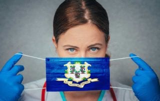 Surgeon With Medical Liability Insurance Placing A Mask With The Connecticut State Flag Over Her Face
