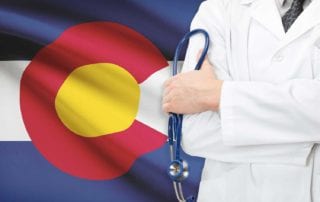 Doctor With Medical Malpractice Insurance Standing In Front Of Colorado State Flag Holding Stethoscope
