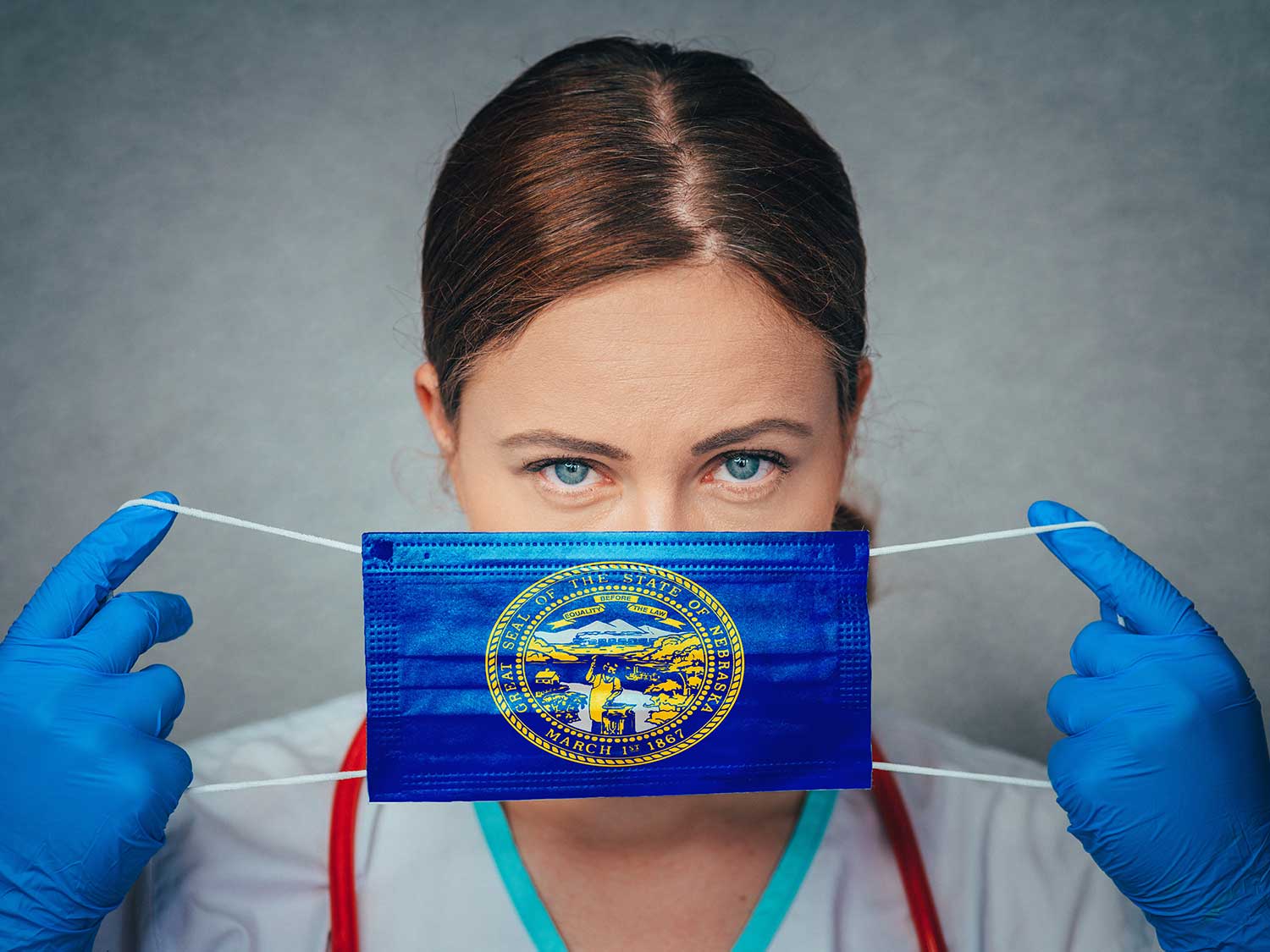 A Female Doctor With Medical Malpractice Insurance Holding A Nebraska State Flag Surgical Mask Over Her Face