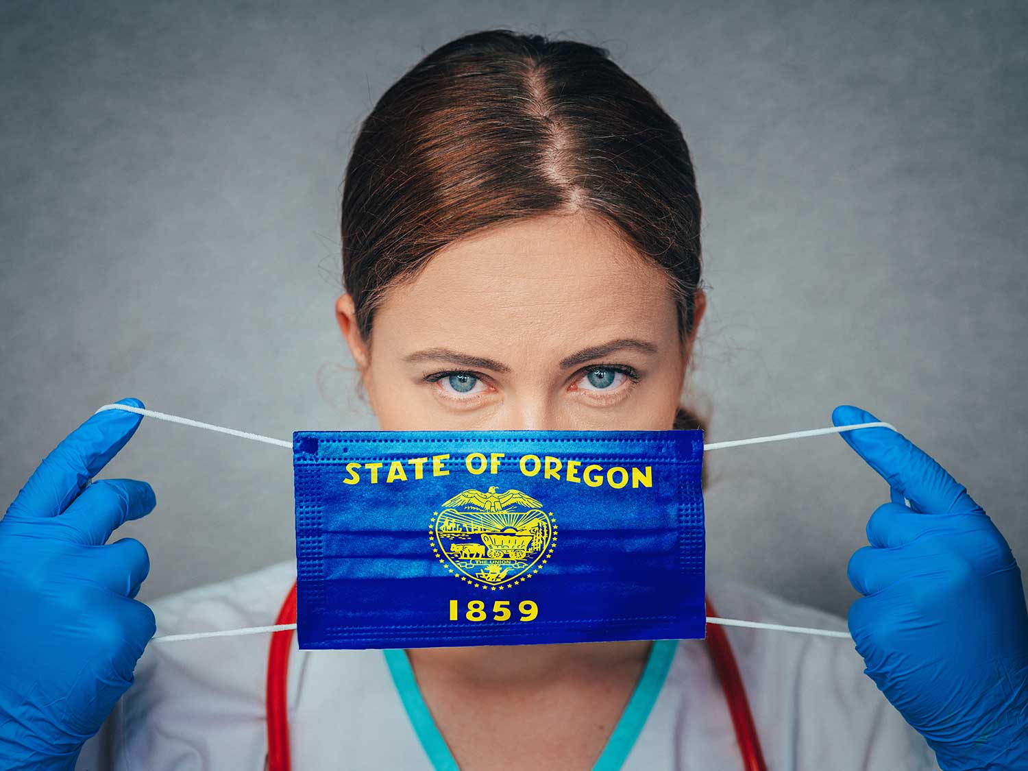 A Female Physician With Medical Malpractice Insurance Holding A Oregon State Flag Surgical Mask Over Her Face